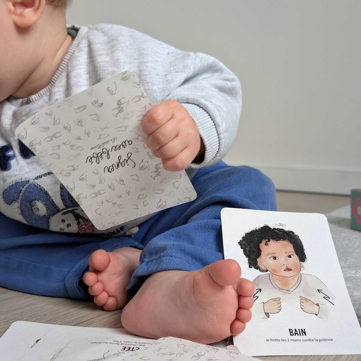 bébé manipule les cartes signer avec bébé, gros plan sur les pieds de bébé et la cartes "bain"