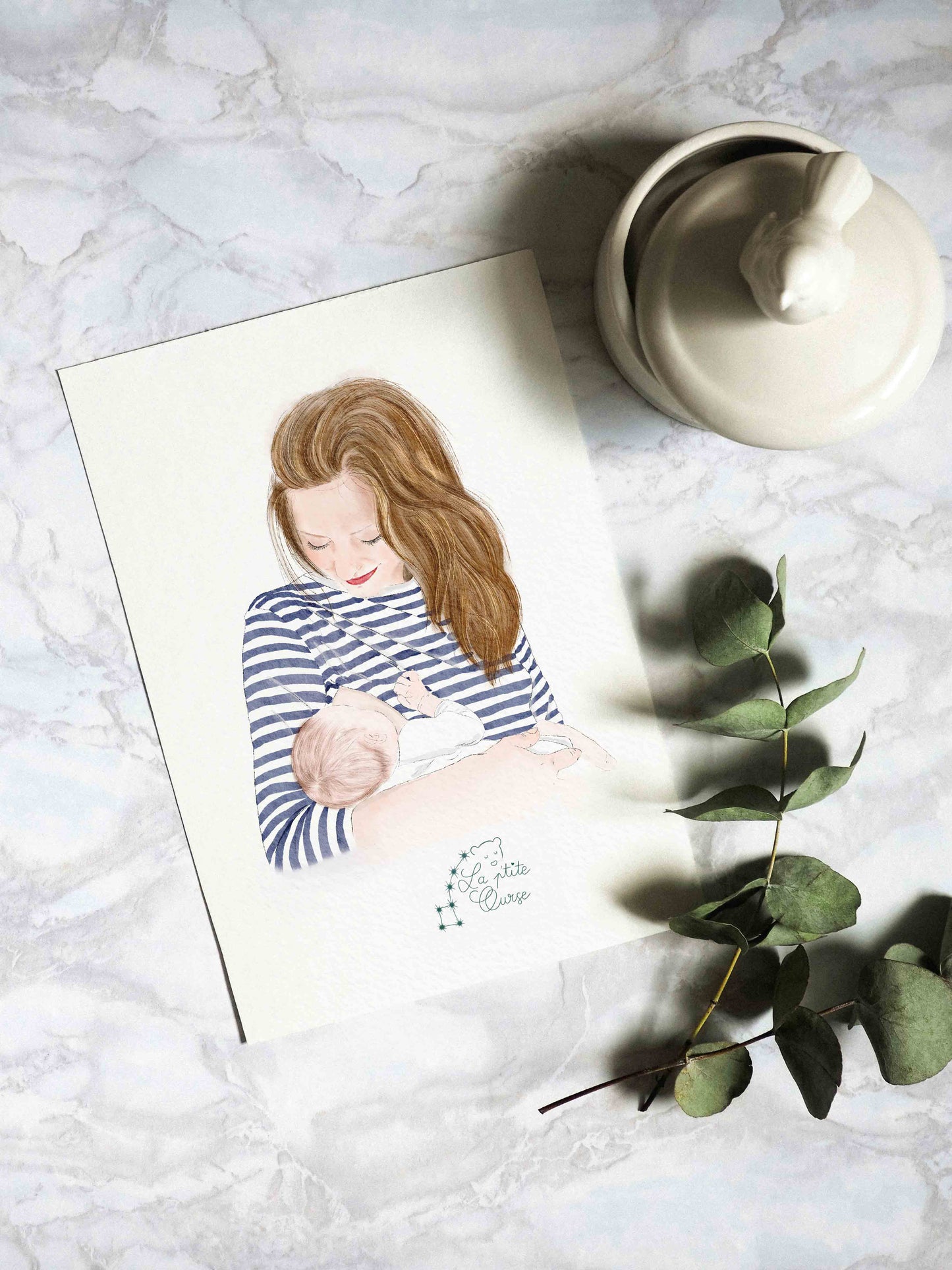 portrait lacté, portrait d'une maman allaitant son bébé présenté sur un support marbré entouré de feuillages d'eucalyptus