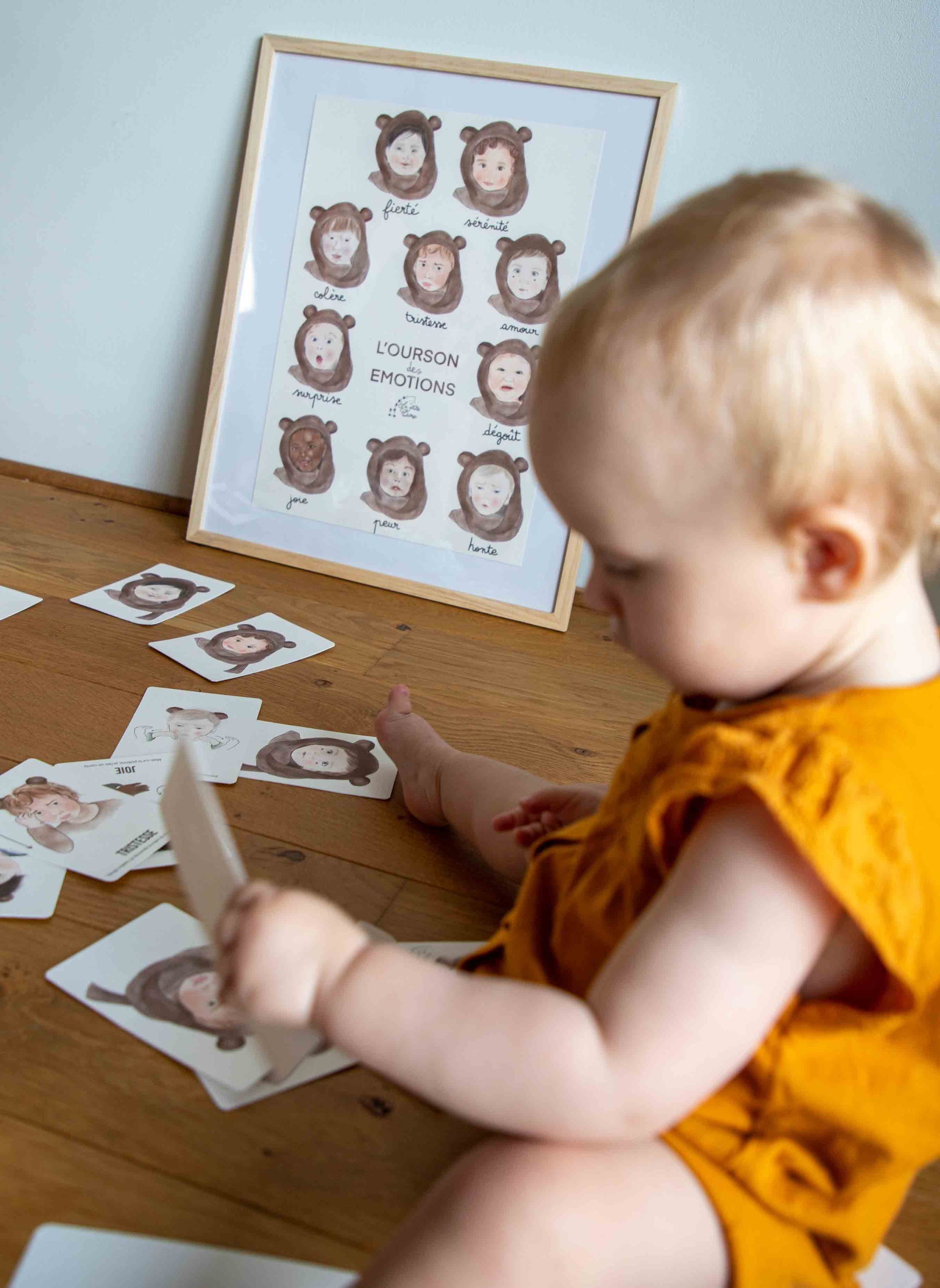 Bébé assis, jouant avec les cartes bébé signes l'ourson des émotions, devant l'affiche bébé signe l'ourson des émotions