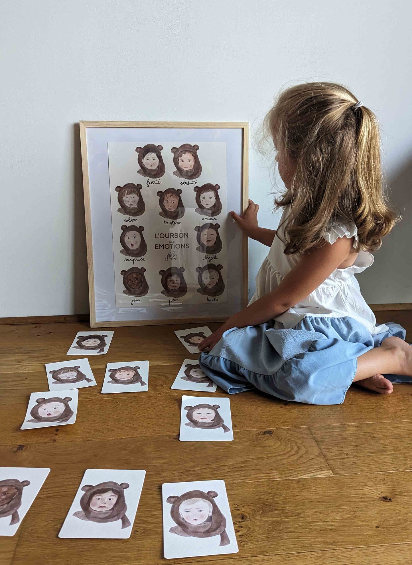 Petite fille assise à côté des cartes bébé signe l'ourson des émotions regardant l'affiche bébé signe l'ourson des émotions