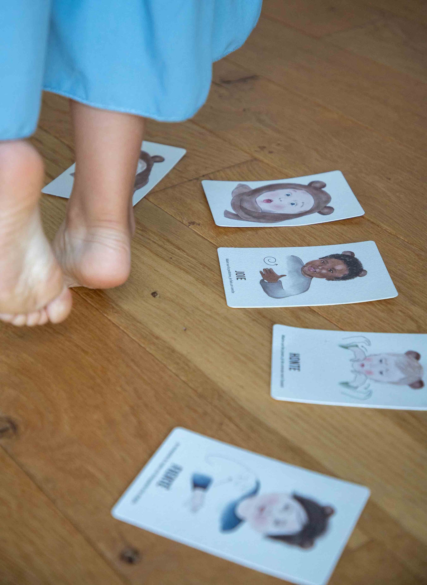 Cartes "Signer avec Bébé les Émotions" posées sur le parquet, laissant apparaître les pieds nus d'un enfant.