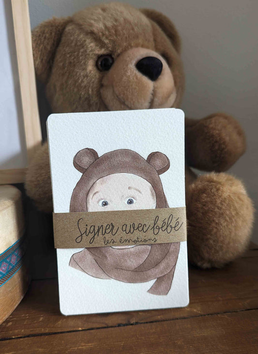Cartes bébé signe "Signer avec Bébé les Émotions" emballées avec un lien en kraft, placées devant un ourson brun.