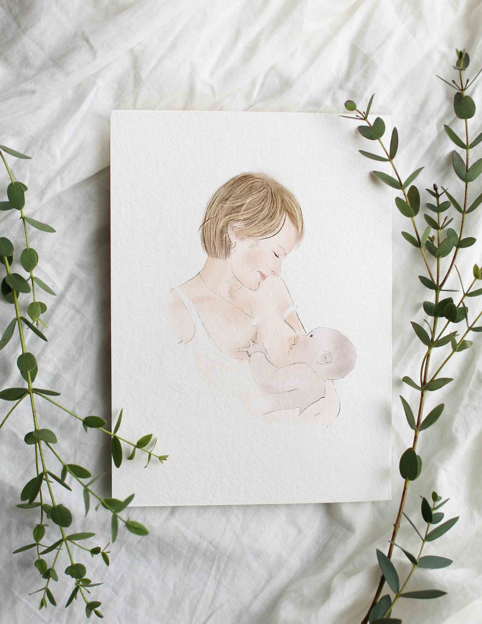 portrait lacté, portrait d'une maman allaitant son bébé présenté sur un drap blanc entouré de feuillages d'eucalyptus